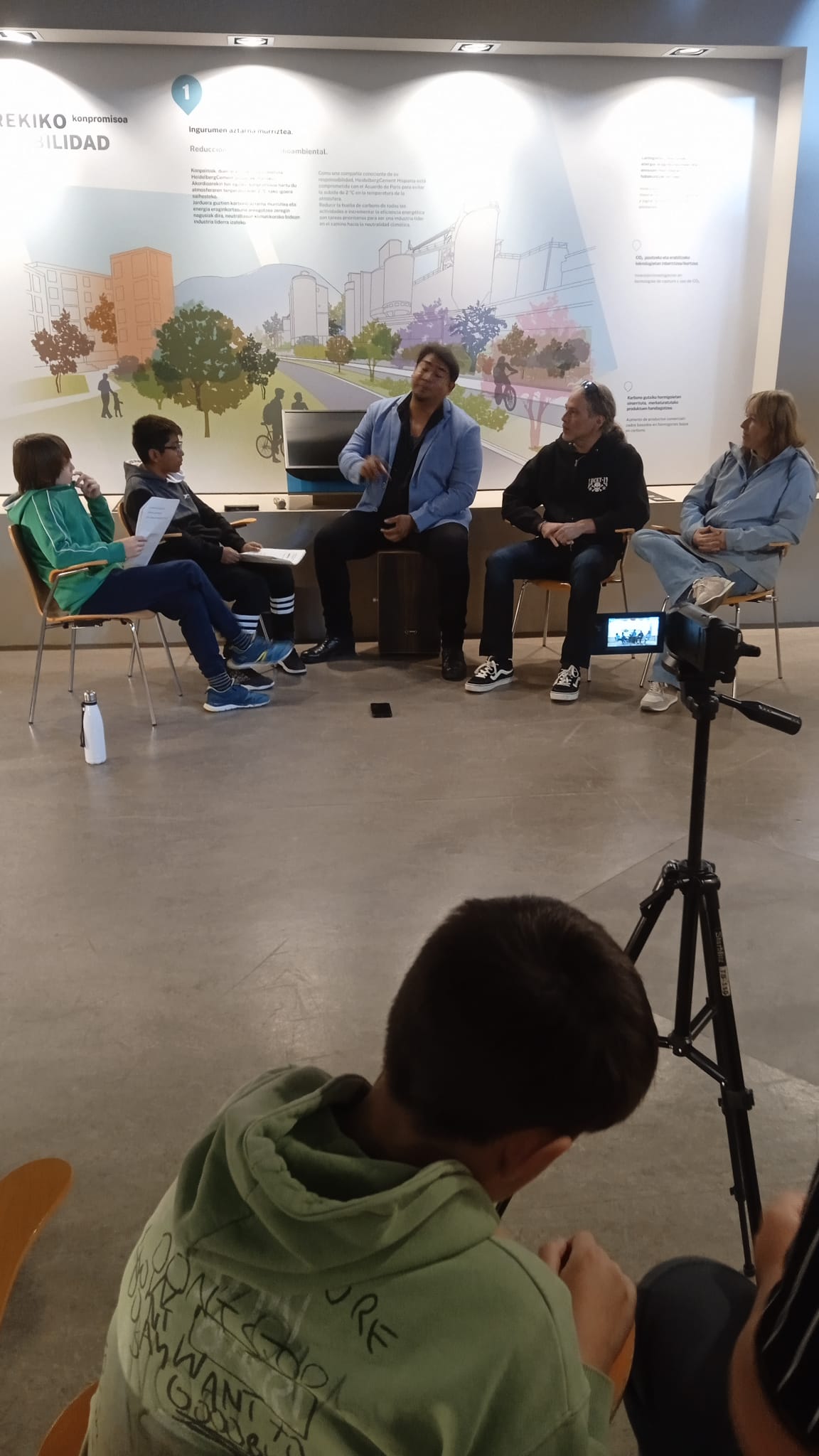 Imagen de una cámara de video y unos jóvenes sentados en una aula.